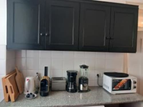 Modern kitchen counter in Lisbon apartment with black cabinets, white backtile, coffee maker, microwave, and appliances