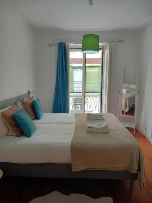 Bright bedroom in Lisbon apartment with double bed, teal pillows, green pendant lamp, and balcony view