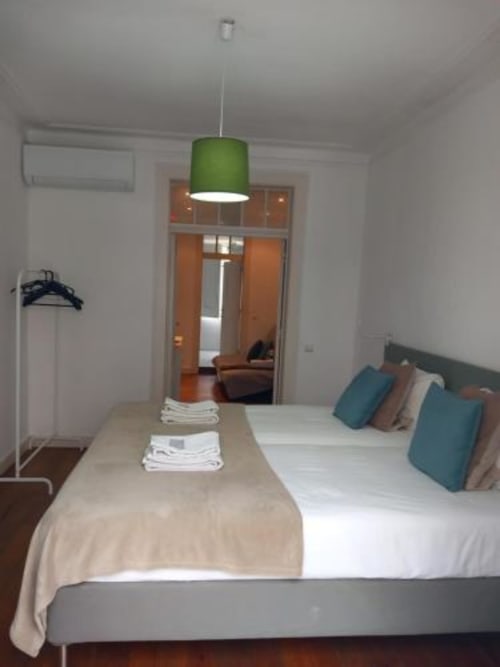 Modern bedroom in Lisbon apartment with green pendant light, white bedding, and open doorway to living area