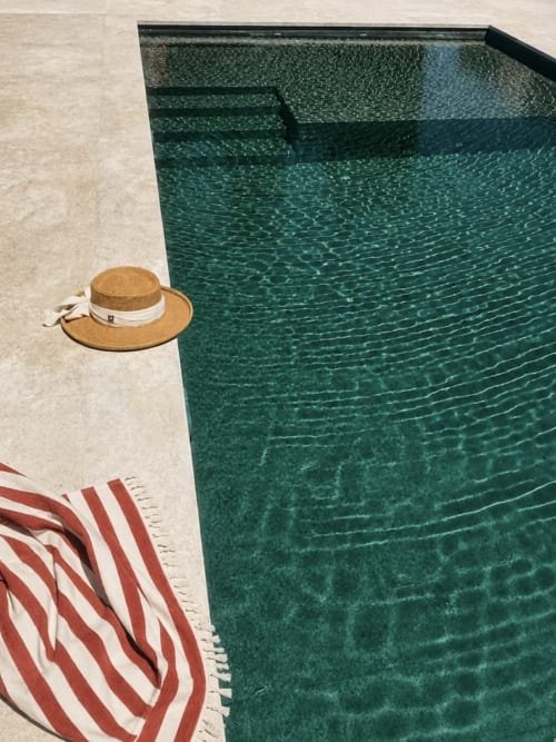 Straw hat and red striped towel beside turquoise pool at Casa Rural Finca El Olivar cottage