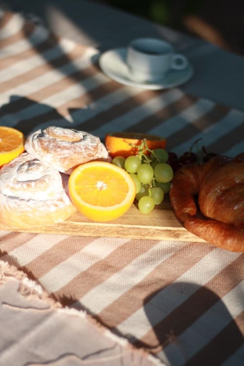 Outdoor picnic setup at Casa Rural Finca El Olivar with fresh bread, oranges, grapes, and pastries on wooden board under