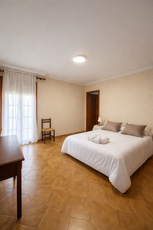 Spacious bedroom at Casa Rural Finca El Olivar with king bed, terracotta floors, and garden views from balcony