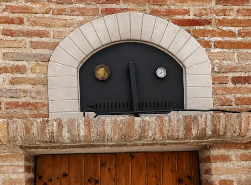 Black fireplace with arched stone surround and decorative accents on brick wall at Casa Rural Finca El Olivar