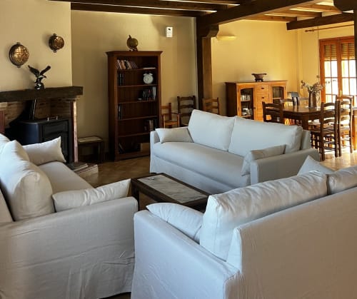 Spacious living room at Casa Rural Finca El Olivar cottage with cream sofas, fireplace, bookshelf, and dining area with