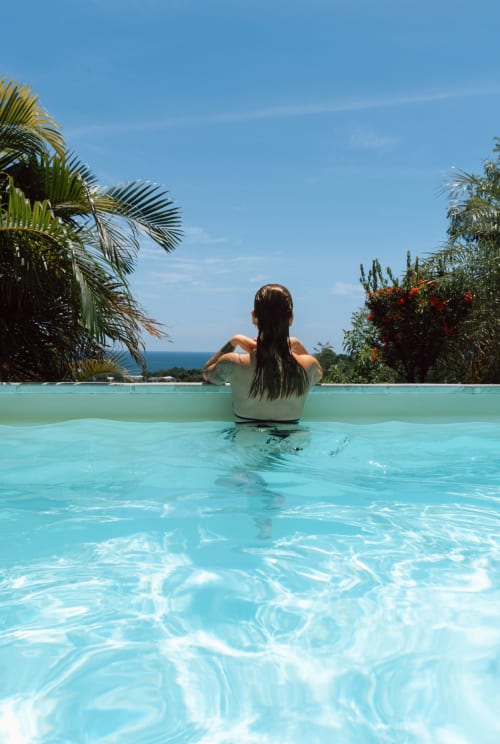 Femme se relaxant dans une piscine à débordement turquoise surplombant la mer des Caraïbes aux Exotic Villas Martinique, Le Diamant
