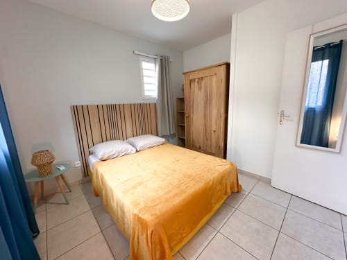 Chambre lumineuse avec tête de lit en bois, courtepointe orange et armoire en bois aux Exotic Villas Martinique au Diamant