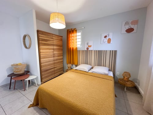 Chambre de la villa Ananas aux Exotic Villas Martinique avec literie jaune, tête de lit en bois, rideaux orange et design moderne