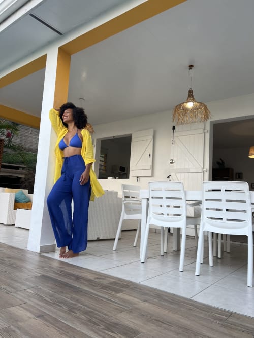 Femme en cardigan jaune sur la terrasse d'une villa Exotic Villas Martinique avec chaises de salle à manger et luminaire pendant doré