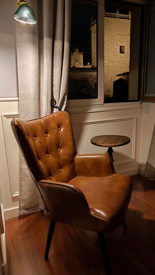 Sillón de cuero tipo wingback con vistas a un monumento medieval de Cáceres desde el apartamento Mirador Medieval