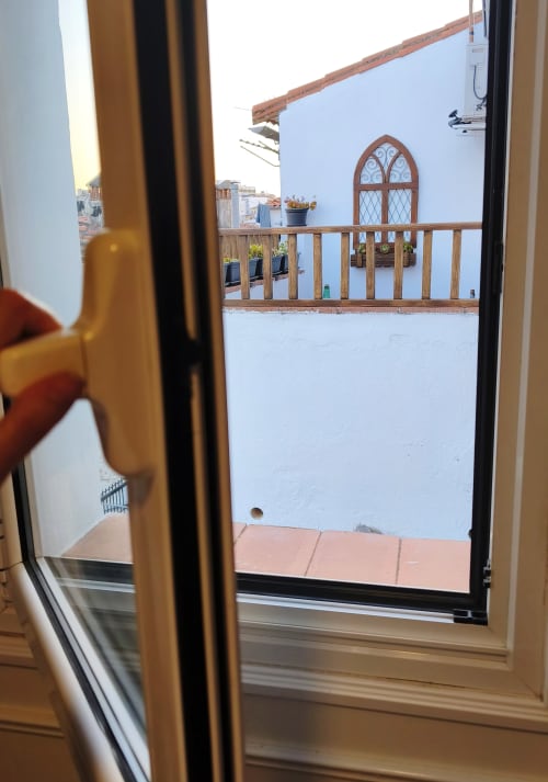 Puerta de madera abierta con vista al emblemático Cáceres medieval, edificio de muros blancos y ventana ornamental