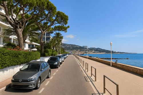 Cannes beachfront promenade with parked cars, palm trees, Mediterranean Sea, and hillside views