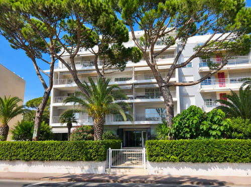 Modern white apartment building in Cannes with palm trees and green hedges, managed by Pascale Beaud