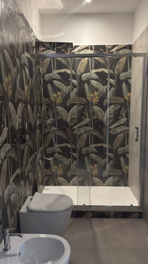 Bagno moderno con carta da parati a foglie di banana tropicali, doccia walk-in e toilette presso la suite BellDuomo di Messina