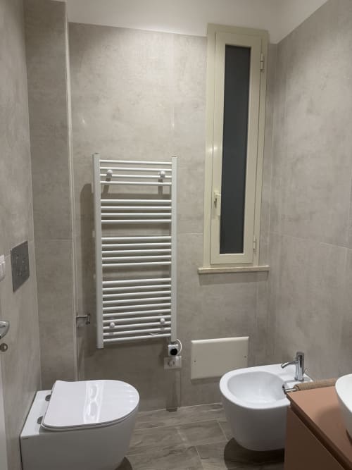 Bagno moderno della Suite BellDuomo a Messina con toilette bianca, lavabo rotondo, scaldasalviette e pareti in piastrelle beige