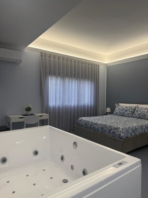 Lussuosa camera da letto BellDuomo Suite Messina con vasca idromassaggio, letto matrimoniale, tende da pavimento a soffitto e illuminazione ambientale