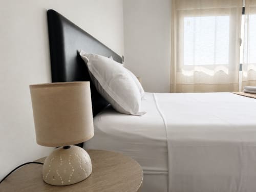Modern bedroom at DakarByDays with beige lamp, black headboard, white pillows, and bright city view in Dakar apartment