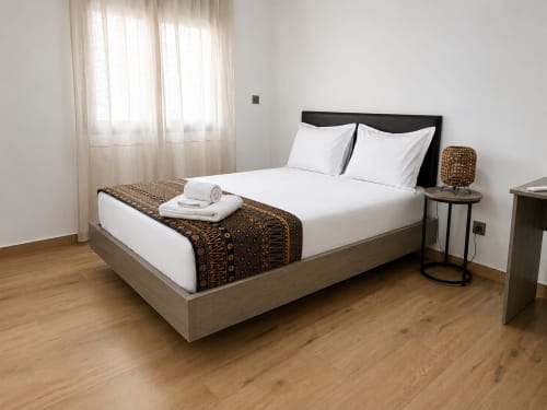 Modern bedroom at DakarByDays apartment in Dakar with queen bed, white linens, woven throw, side tables, and natural light