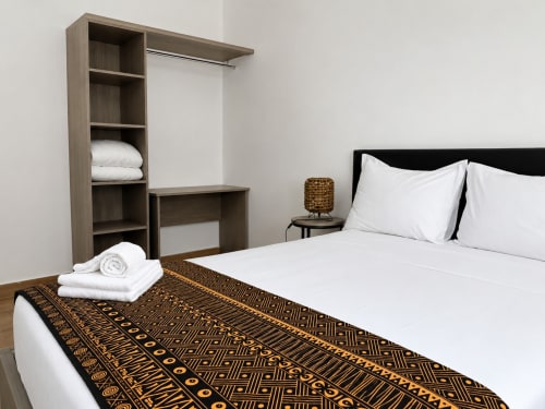 Modern bedroom in Dakar apartment with white linens, patterned throw, wooden built-in wardrobe, and desk
