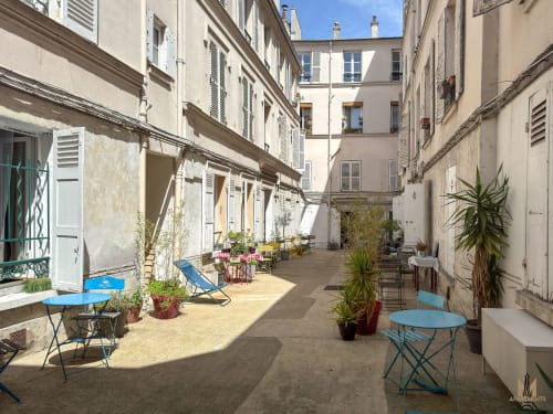 Charmante cour des Appartements Montmartre Paris, avec mobilier de café bleu, plantes en pots et bâtiments parisiens classiques