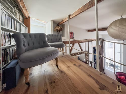Appartement parisien moderne à Montmartre avec fauteuil gris, bureau en bois, poutres apparentes et mezzanine