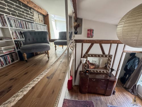 Coin salon d'appartement à Montmartre avec chaises sombres, bibliothèque, poutres en bois et mobilier d'époque à Paris