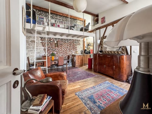 Appartement Del Sarte à Montmartre, Paris : fauteuil cuir, briques apparentes, chambre mezzanine, poutres bois, décor éclectique