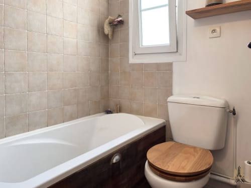 Salle de bain moderne avec baignoire blanche, toilettes à siège bois et carrelage beige aux Appartements Montmartre, Paris