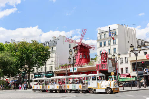 Scène pittoresque à Montmartre, Paris : le célèbre cabaret Moulin Rouge rouge vif, bâtiments blancs et petit train touristique