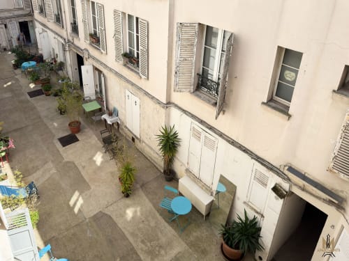 Cour d'immeubles à Montmartre, Paris, avec sièges bleus, plantes en pots et façade couleur crème