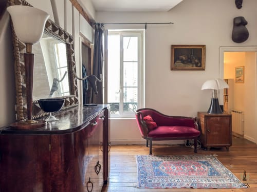 Élégant salon d'appartement parisien avec canapé velours bordeaux, miroir ouvragé, bureau en bois et mobilier d'époque
