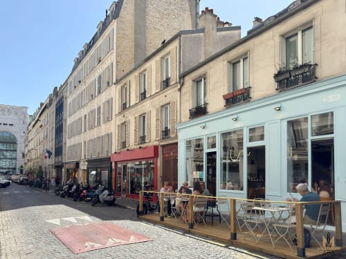 Charmante scène de rue parisienne à Montmartre avec bâtiments historiques, terrasse de café et devanture bleue ciel
