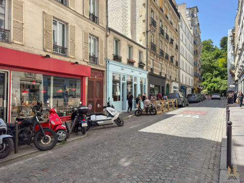 Rue pittoresque de Montmartre avec terrasses de cafés, scooters et bâtiments haussmanniens historiques sous ciel bleu