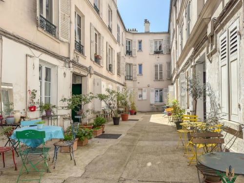 Cour parisienne pittoresque aux Appartements Montmartre avec chaises de bistrot colorées, plantes en pot et architecture Haussmann classique