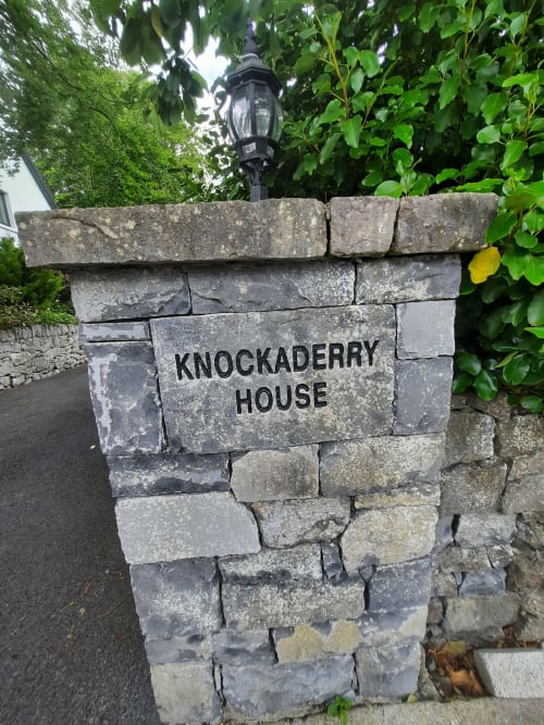 Stone entrance sign for Knockaderry House B&B in Ennis, Ireland, with lamp and ivy