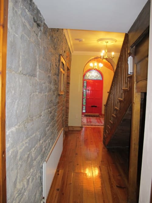 Knockaderry House hallway in Ennis with stone walls, wooden floors, and a distinctive red arched entrance door