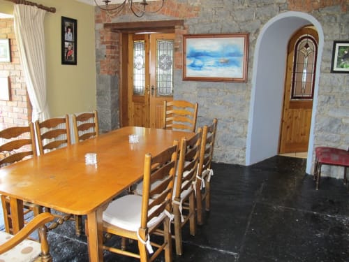 Knockaderry House dining room in Ennis with wooden table, ladder-back chairs, stone walls, and arched doorway.