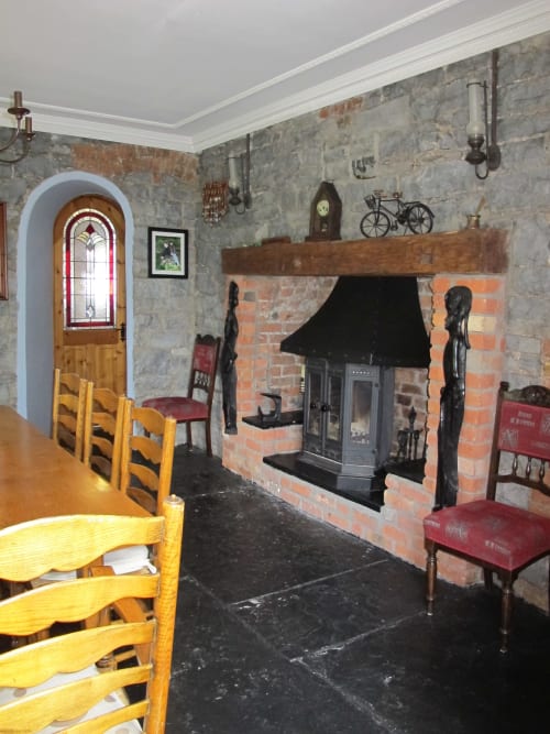 Knockaderry House dining room with fireplace, stove, wooden chairs, and arched doorway in Ennis, Ireland