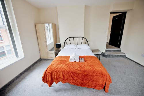 Modern bedroom at The JS Apartments in Blackburn with city view, orange throw, black metal bed frame and wooden furniture