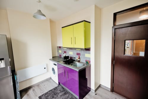 Modern kitchen in The Residence by JS Apartments Blackburn, featuring yellow and purple cabinets, colorful backsplash, and