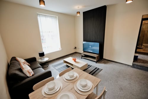 Modern open-plan apartment at The JS Apartments, Blackburn featuring dining table, black sofa, TV and city view from window