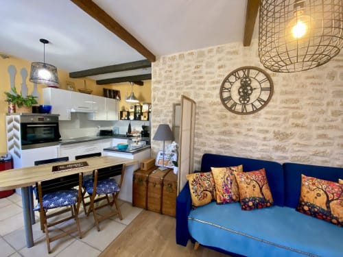 Le Cocon Boheme à Sarlat : cuisine ouverte et séjour avec canapé bleu, poutres apparentes, murs de brique et coloré