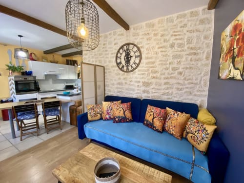 Salon bohème cosy avec canapé bleu, poutres apparentes et cuisine à Sarlat, France