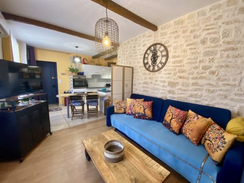 Salon bohème cosy avec canapé bleu, cuisine, briques apparentes et horloge décorative à Sarlat