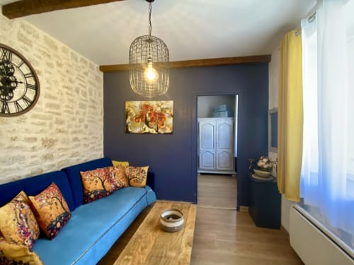 Séjour bohème cosy à Ô Clair De Lune à Sarlat avec canapé bleu, coussins à motifs, luminaire suspendu et poutres en bois