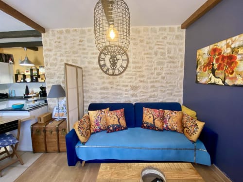 Salon bohème cosy avec canapé bleu velours, coussins colorés, murs en brique et lampe suspendue à Sarlat, France
