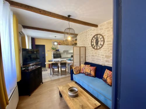 Salon du gîte Le Cocon Boheme avec canapé bleu, kitchenette, TV et poutres apparentes à Sarlat
