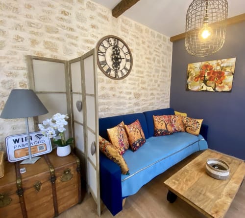 Chambre bohème chaleureuse à Sarlat : canapé bleu marine, coussins dorés, horloge vintage et murs en brique