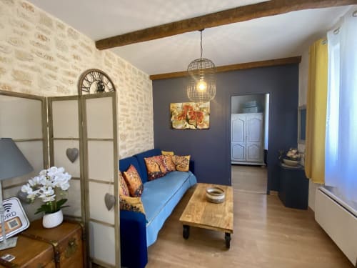 Salon chaleureux du gîte Ô Clair De Lune, Sarlat : canapé bleu, poutres en bois et murs en pierre rustique
