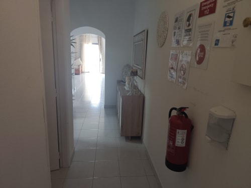 Corredor da Albufeira Inn com extintor de incêndio, cartazes de segurança e luz natural da entrada