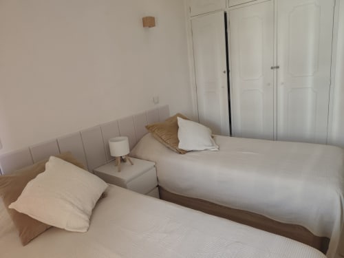 Dois camas individuais com roupa branca num quarto limpo da Albufeira Inn, Edifício Elimar 1, com luminária na mesinha de cabeceira e